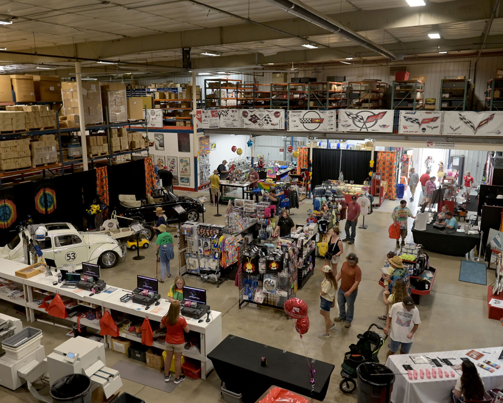 Funfest warehouse area with Herbie display vendors and attendees exploring event merchandise